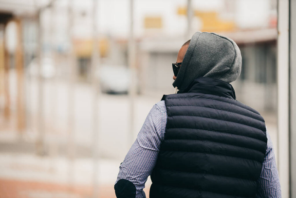 A rearview of a guy with a hood wearing a shirt, vest jacket, and sunglasses - Foto, afbeelding
