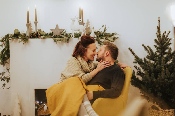 Merry Christmas and Happy Holidays! Young couple having fun near fireplace and Christmas tree indoors. Loving family in a cozy atmosphere - 写真・画像