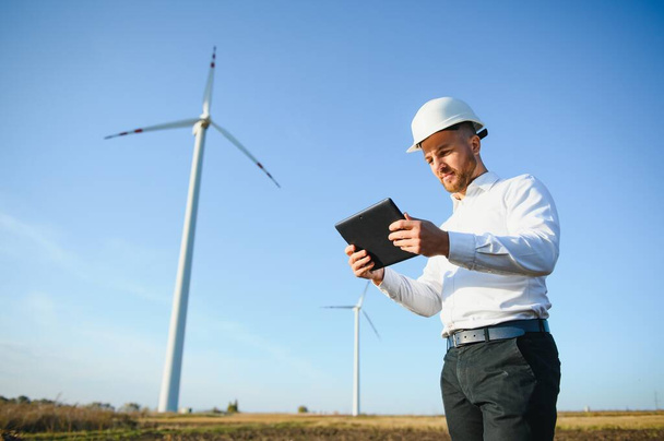 Young engineer man looking and checking wind turbines at field - Fotoğraf, Görsel