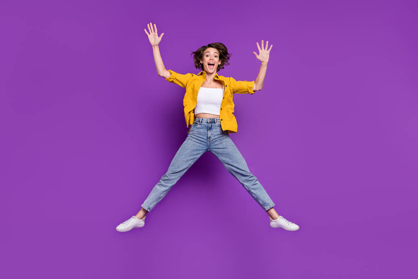 Photo of charming funny young lady wear yellow shirt jumping high smiling isolated violet color background - Fotoğraf, Görsel