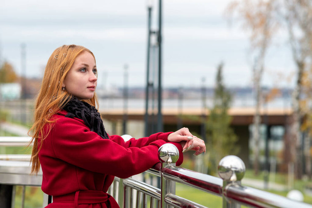 bella ragazza dai capelli rossi guarda in lontananza mentre in piedi sopra l'argine della città di autunno - Foto, immagini