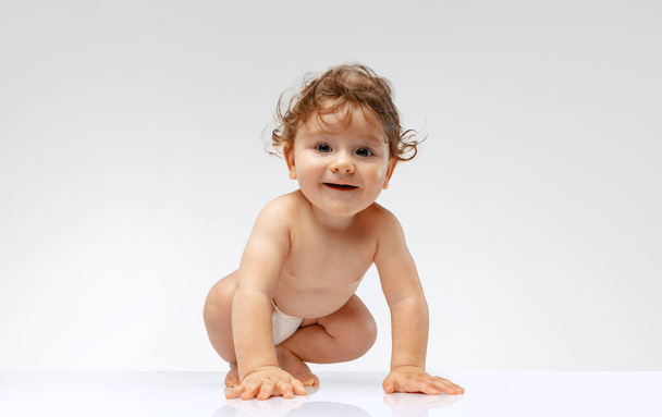 Moving. Playful baby. Portrait of cute beautiful toddler boy, baby in diaper crawling isolated over white studio background. Concept of childhood, motherhood, life, birth. Copy space for ad - Foto, Imagen