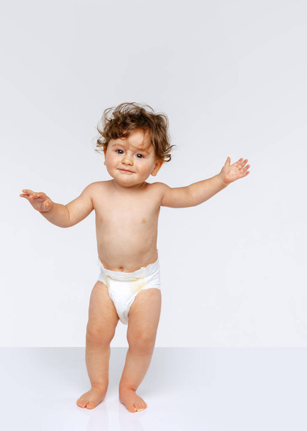 Κάνω τα πρώτα βήματα. Πορτρέτο του χαρούμενου μικρού αγοριού, μωρό σε πάνα με τα πόδια απομονωμένο πάνω από λευκό φόντο στούντιο. Έννοια της παιδικής ηλικίας, μητρότητα, ζωή, γέννηση. Αντιγραφή χώρου για διαφήμιση - Φωτογραφία, εικόνα