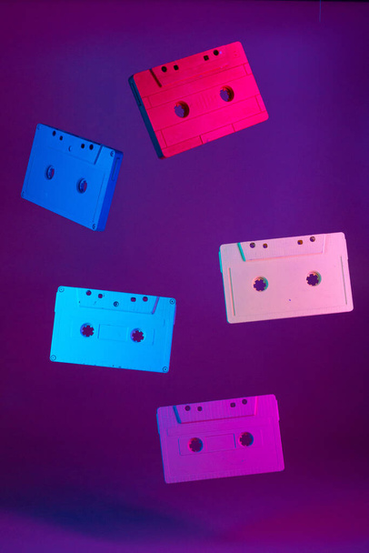 Colored audio cassettes hanging in the air against purple background - Fotó, kép