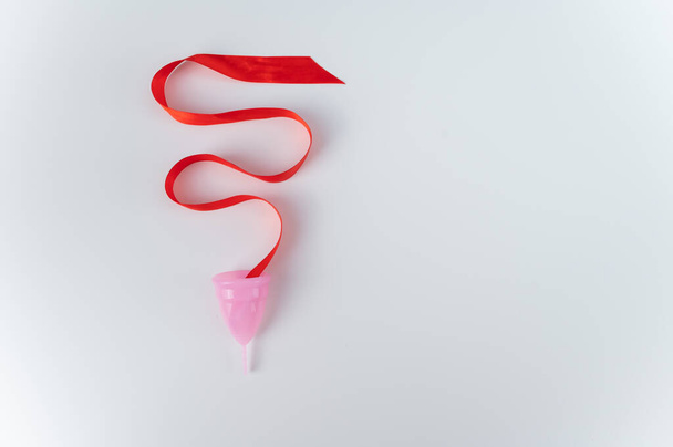 Pink menstrual cup and red satin ribbon on a white background. Copy space. - Fotografie, Obrázek