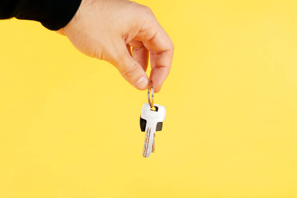 mano sosteniendo las llaves de la casa, sugiriendo, sobre fondo amarillo. - Foto, Imagen