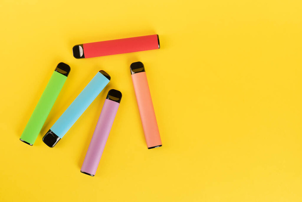 Διάταξη πολύχρωμων ηλεκτρονικών τσιγάρων μιας χρήσης σε κίτρινο φόντο. Η έννοια του σύγχρονου καπνίσματος, ατμίσματος και νικοτίνης. - Φωτογραφία, εικόνα