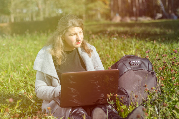Retrato de uma bela mulher de meia-idade com cabelo comprido que está trabalhando em um laptop. ela está sentada na grama verde no parque da cidade. - Foto, Imagem
