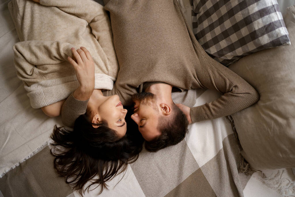 Beautiful young happy couple relaxing in bed and smiling, embracing - 写真・画像