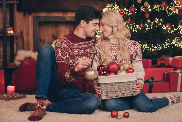 Portrait of two attractive sweet tender dreamy married spouses sitting on carpet decorating fir tree newyear custom indoors - 写真・画像