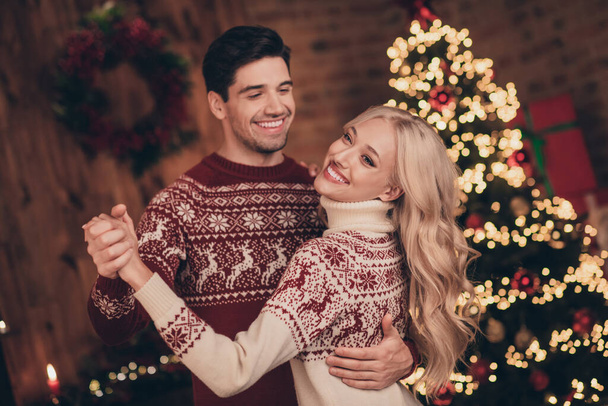 Zdjęcie dość podekscytowany żona mąż ubrany druk pulowerów taniec świętowanie Bożego Narodzenia uśmiechając się w pomieszczeniu domu - Zdjęcie, obraz