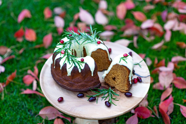 Vánoční karamelový dort, odřezky, zdobený bílou čokoládou, brusinkami a rozmarýnem na dřevěném stojanu mezi podzimními listy. Sváteční pečivo. Měkké selektivní zaměření. Vodorovně - Fotografie, Obrázek