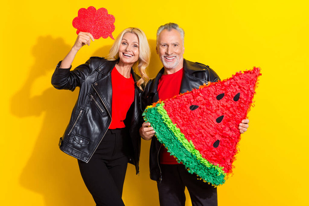 Portrait of beautiful handsome pensioner cheery grey-haired friends holding artificial piece fruit isolated over bright yellow color background - Fotó, kép