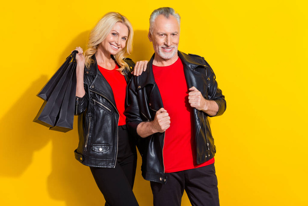 Portrait of attractive cheerful cool grey-haired spouses buying goods clothes isolated over bright yellow color background - Foto, imagen