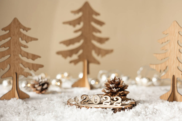 Año nuevo 2022. Números 2022 en soporte de madera sobre fondo borroso pastel beige con abetos decorativos, nieve y luces. Tarjeta de felicitación de Navidad. - Foto, imagen