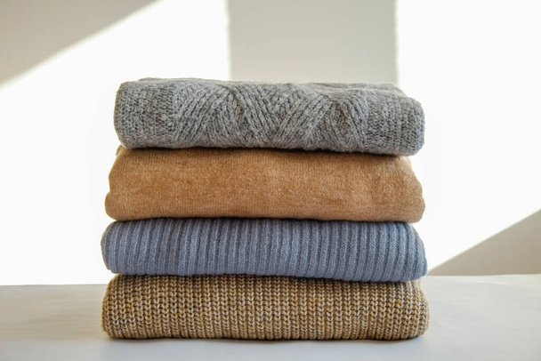 Bunch of knitted warm pastel color sweaters with different knitting patterns folded in stack, clearly visible texture. Stylish fall-winter season knitwear clothing. Close up, copy space for text. - Foto, imagen
