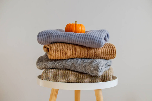 Bunch of knitted warm pastel color sweaters with different knitting patterns folded in stack, visible texture. Stylish fall-winter season knitwear with pumpkin on top. Close up, copy space for text. - Zdjęcie, obraz