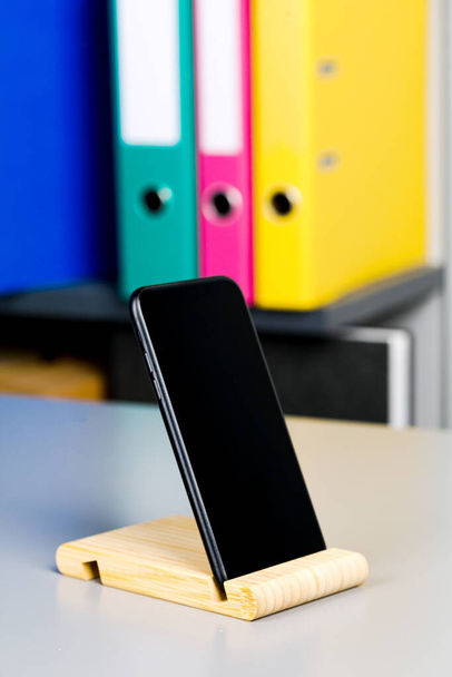 Auf dem Tisch liegt ein schwarzes Smartphone auf einem Holzständer. Ein Ort zum Kopieren. - Foto, Bild
