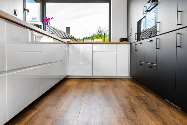 Een moderne keuken met witte en zwarte fronten en een groot hoekraam, vinyl panelen op de vloer. - Foto, afbeelding