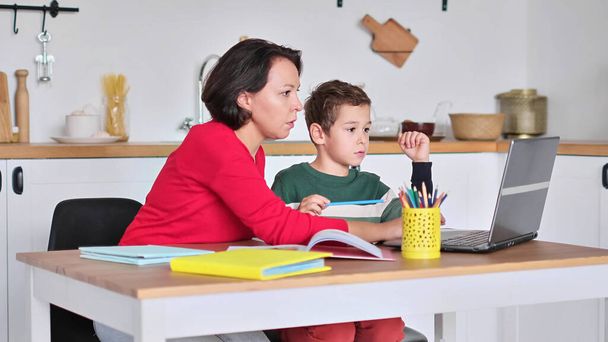 Female private tutor helping young student with homework at desk in bright childs room. mother helps son to do lessons. home schooling, home lessons. - Photo, Image