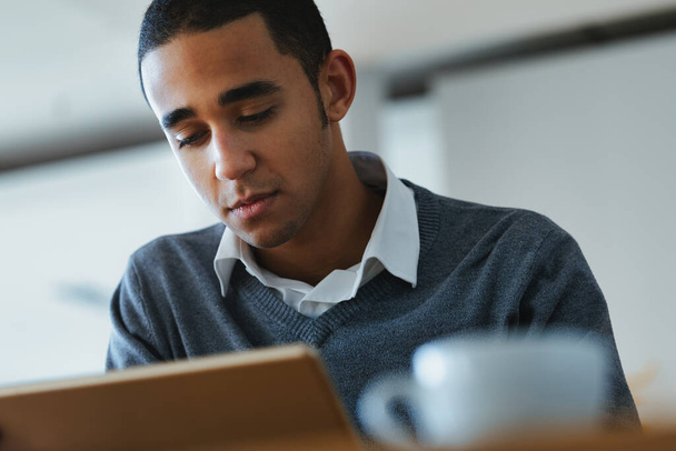 Серйозний молодий чорний чоловік захопився читанням на планшетному ПК у крупним планом з низьким кутом зору
 - Фото, зображення
