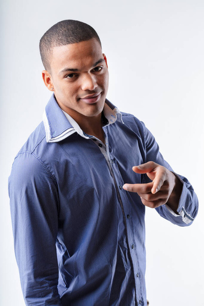 Молодой модный умный чёрный мужчина, работающий с камерой, указывая пальцем и улыбаясь на белом фоне студии. - Фото, изображение
