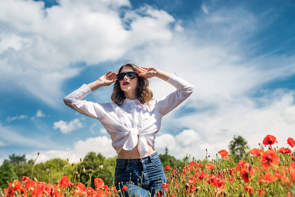Beautiful young girl in the poppy field. She spending free time and good weather for enjoys - Photo, Image