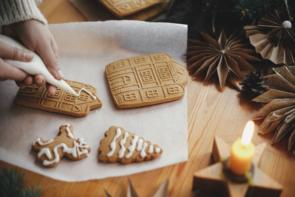 Díszítő karácsonyi mézeskalács cookie-k cukormázzal fából készült asztalra gyertya és díszek. Közel ahhoz, hogy mézeskalács ház cukormázzal. Légköri szeszélyes kép. Üdülési előkészületek - Fotó, kép