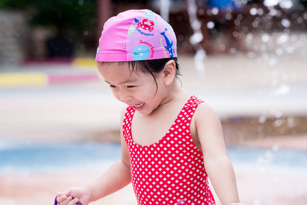 Retrato de niña linda feliz jugando agua. Niño con traje de baño rojo y sombrero de baño rosa. Chico sonrisa dulce es divertido. En verano. - Foto, Imagen