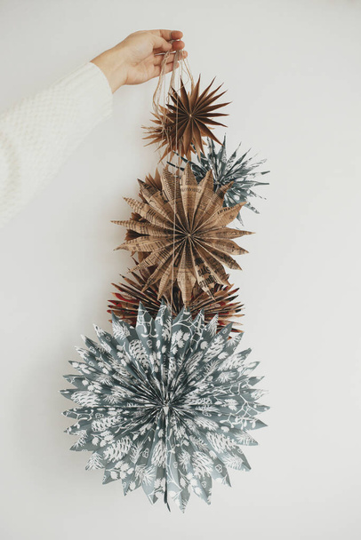 Hand holding many stylish Christmas stars on white wall. Modern festive scandinavian decor in room. Simple sweden paper stars. Winter holiday preparations. Merry Christmas! - Photo, Image