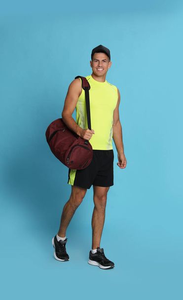 Handsome man with sports bag on light blue background - Foto, imagen