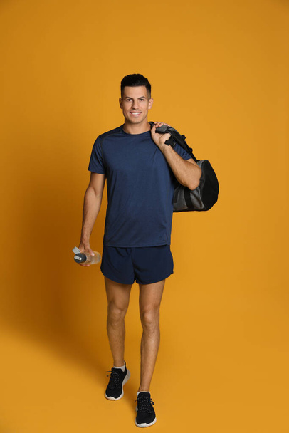 Handsome man with sports bag and bottle of water on yellow background - Foto, Imagem