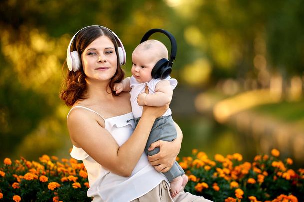 Woman with infant are listening to music with wireless headphones outdoors. - Foto, imagen