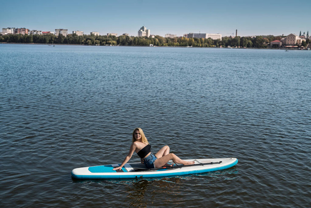 Όμορφο κορίτσι σε μια σανίδα κουπί στη λίμνη της πόλης. καλοκαιρινό τρόπο ζωής  - Φωτογραφία, εικόνα