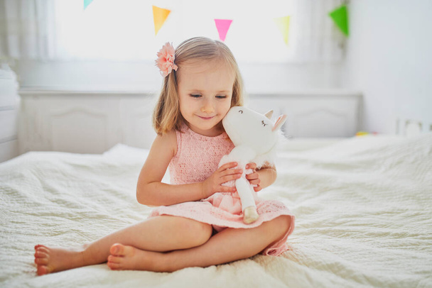 Adorable little girl in pink dress playing with unicorn. Kid having fun with soft toy. Child playing with stuffed toy - Valokuva, kuva