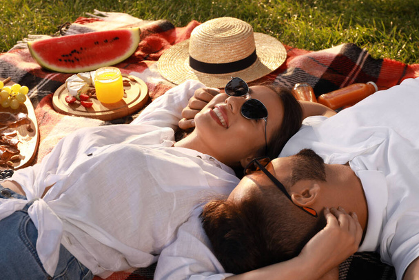 Happy young couple resting on picnic plaid outdoors - Fotó, kép