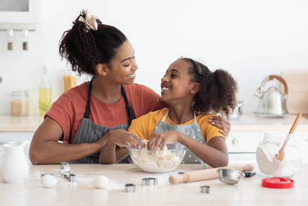 Cute smiling african american mother and daughter cuddling while baking - Photo, Image
