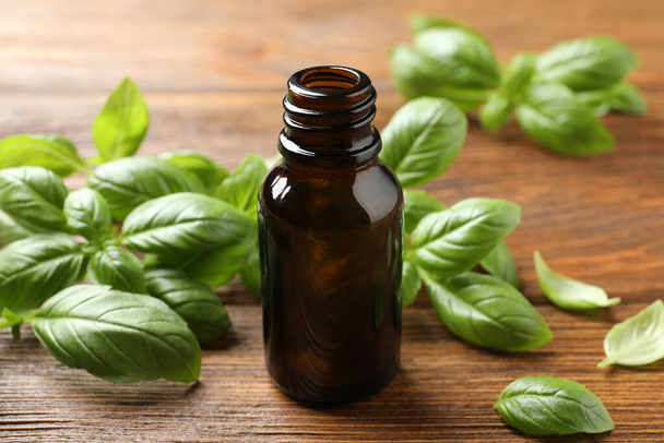 Glass bottle of basil essential oil and leaves on wooden table - Фото, зображення