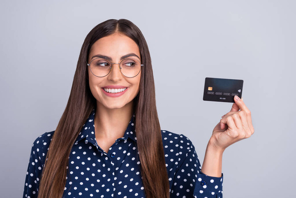 Photo of curious smart banker lady hold credit card look side wear specs dotted blouse isolated grey color background - Fotografie, Obrázek