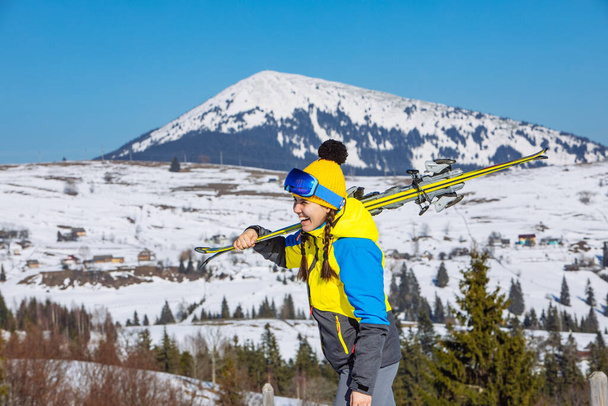 若い笑顔の可愛い女がスキーを持ってる山を背景に冬の旅行 - 写真・画像