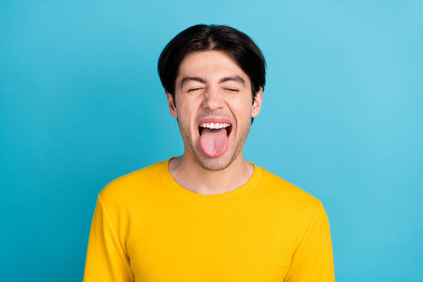 Photo of young man happy positive smile fooling grimace tongue-out isolated over blue color background - Photo, Image