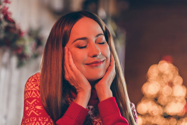 Foto de mujer joven soñadora reflexiva vestida suéter rojo celebrando año nuevo ojos cerrados sonriendo en el interior habitación casa - Foto, imagen