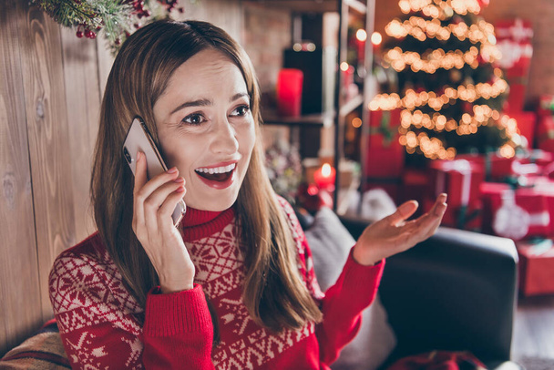 Foto van onder de indruk glanzende jonge vrouw gekleed rode trui praten modern apparaat nieuwjaar groeten glimlachen binnen kamer huis - Foto, afbeelding