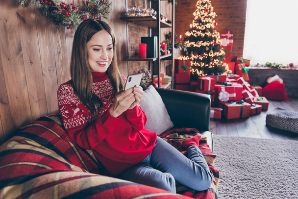Photo of shiny sweet young woman dressed red sweater typing modern device new year congratulations smiling indoors room home house - Foto, Bild