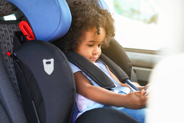 Little African-American girl with mobile phone watching cartoons in car safety seat - Fotó, kép
