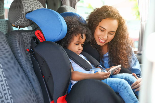 African-American woman and her little daughter watching cartoons in car safety seat - Фото, изображение
