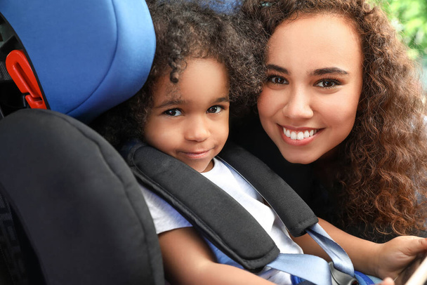 Αφρο-αμερικανική γυναίκα και η μικρή της κόρη δεμένοι σε κάθισμα ασφαλείας αυτοκινήτου - Φωτογραφία, εικόνα
