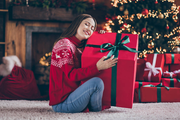 Photo of dreamy sweet young woman dressed red sweater embracing new year big gift box smiling indoors room home house - Foto, Bild