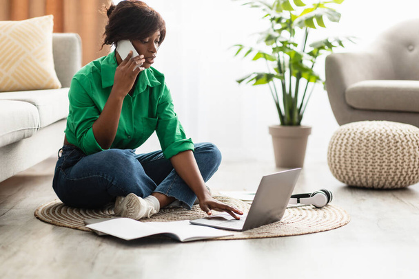Африканська американська жінка розмовляє по телефону, користуючись ноутбуком удома - Фото, зображення