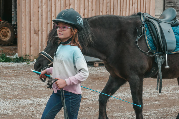 Beautiful horses on a farm in Austria. Little girl goes in for equestrian sports. The child is riding a horse. - Photo, Image